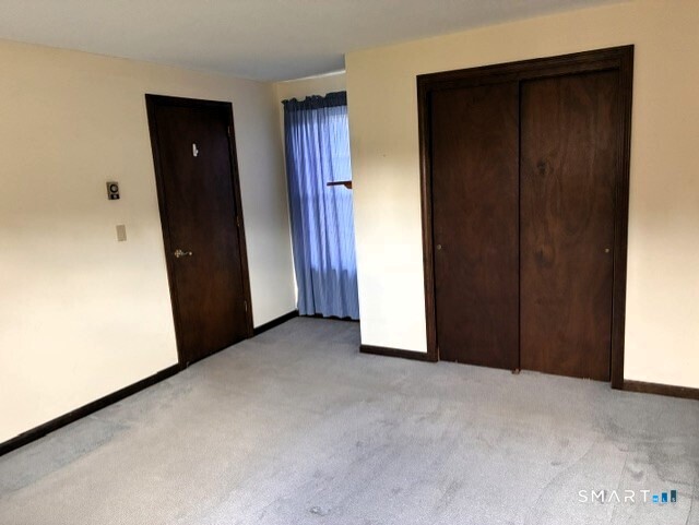 Empty carpeted bedroom with dark wood closet doors and blue curtains.