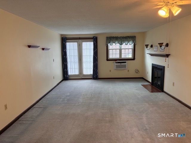 Vacant living room with sliding glass doors, window air conditioner, and corner fireplace.