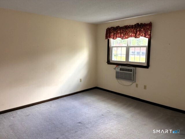 Empty carpeted room with burgundy curtains and a window air conditioner.