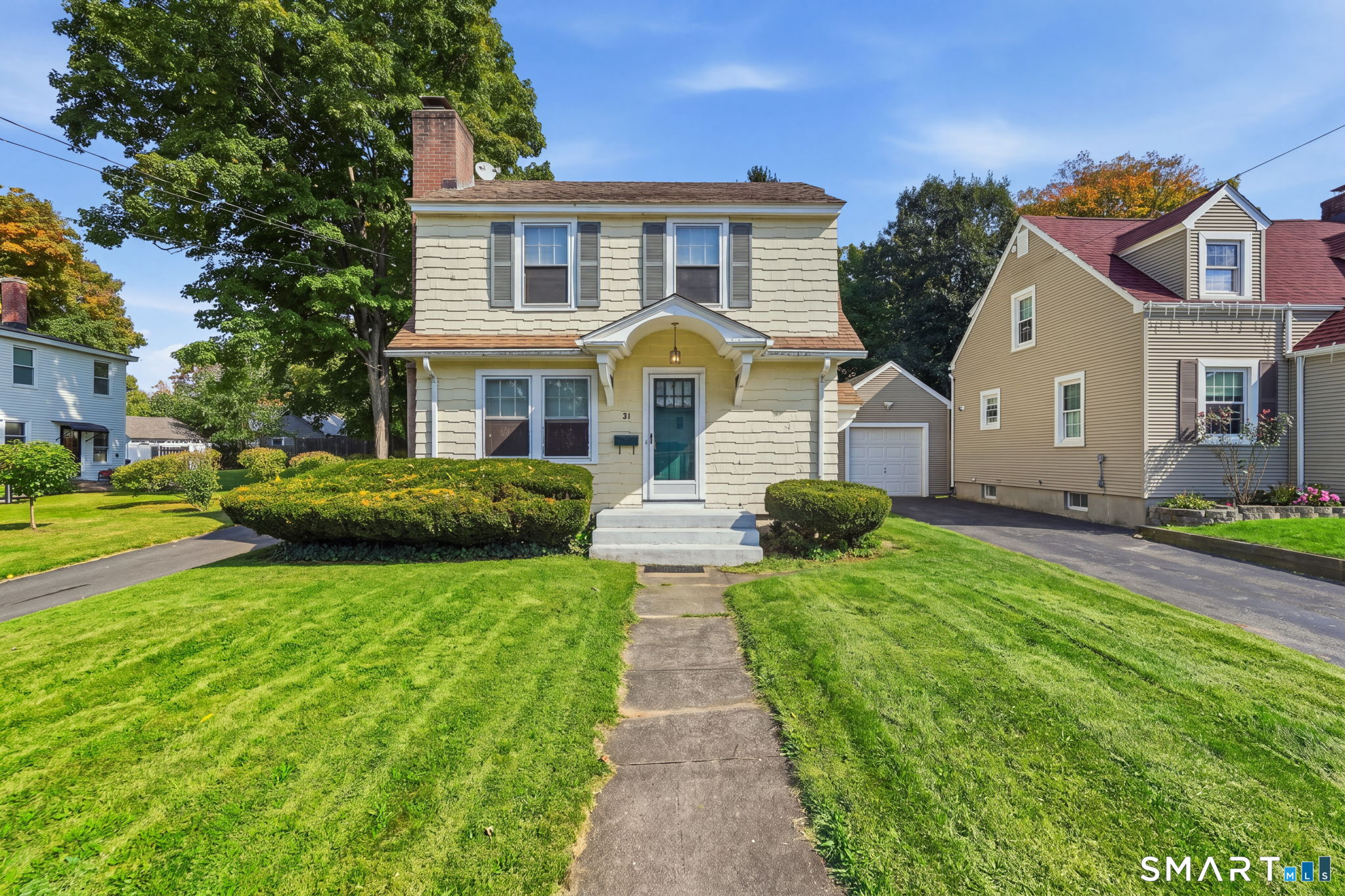 Two-story pale yellow house with an arched porch, teal door, and walkway through a neatly landscaped lawn.