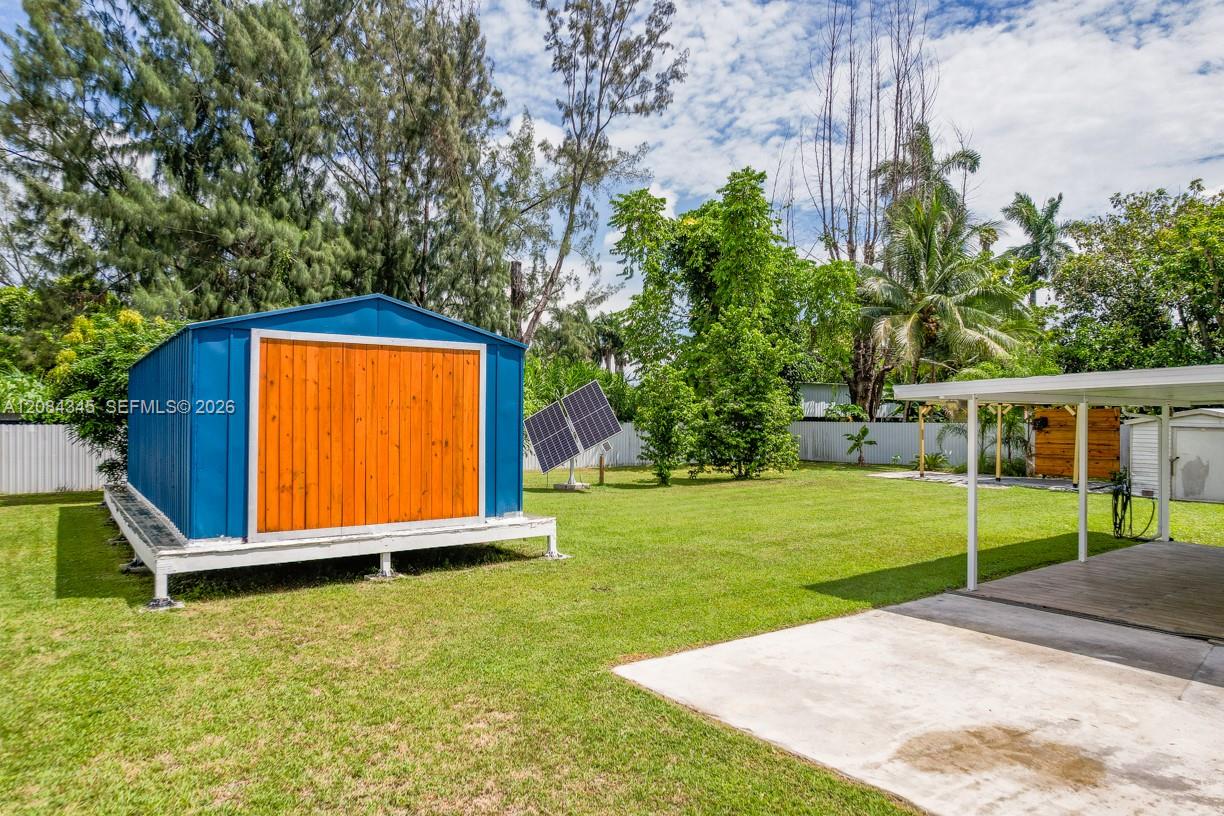 Backyard with a blue shed, orange double doors, solar panel, and covered carport.