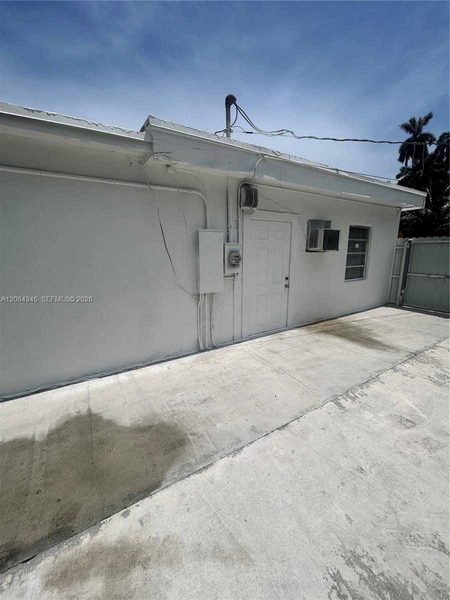 White property's side entrance with a paneled door, window air conditioner, and concrete driveway.