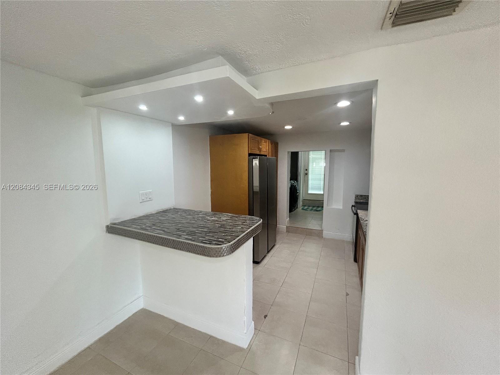Kitchen with a tiled pass-through bar, recessed lights, and stainless-steel refrigerator.