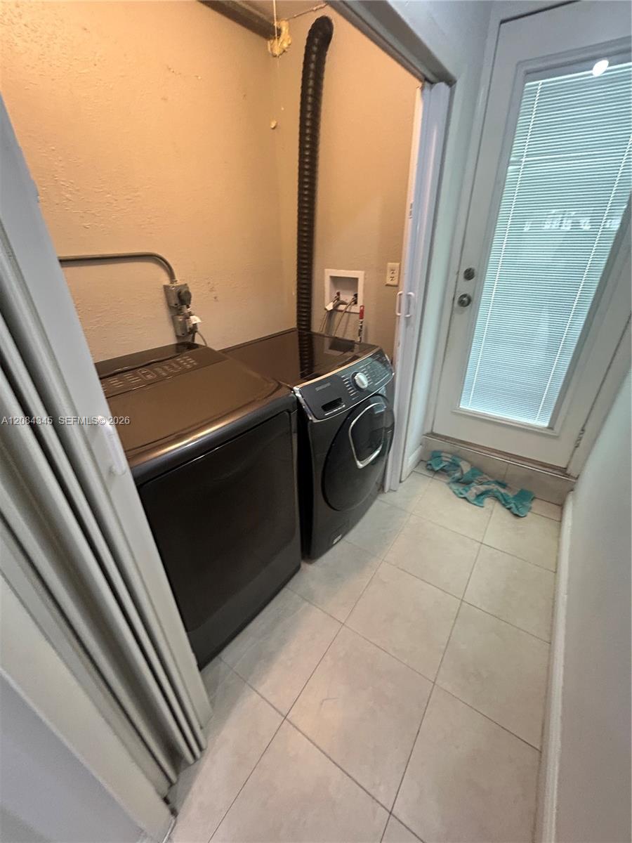 Laundry room with matching dark washer and dryer beside a glass door with blinds.