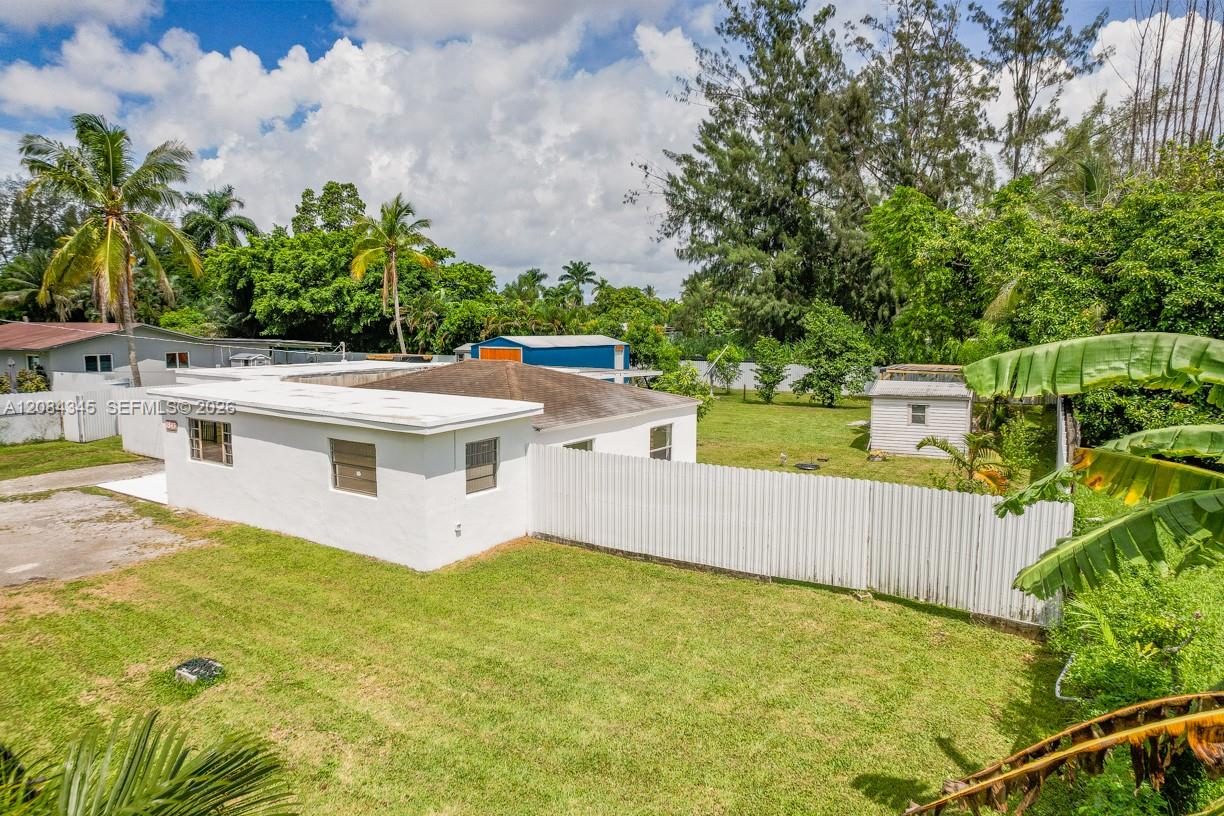Aerial view of a single-story white house and fenced grassy yard surrounded by palm trees.