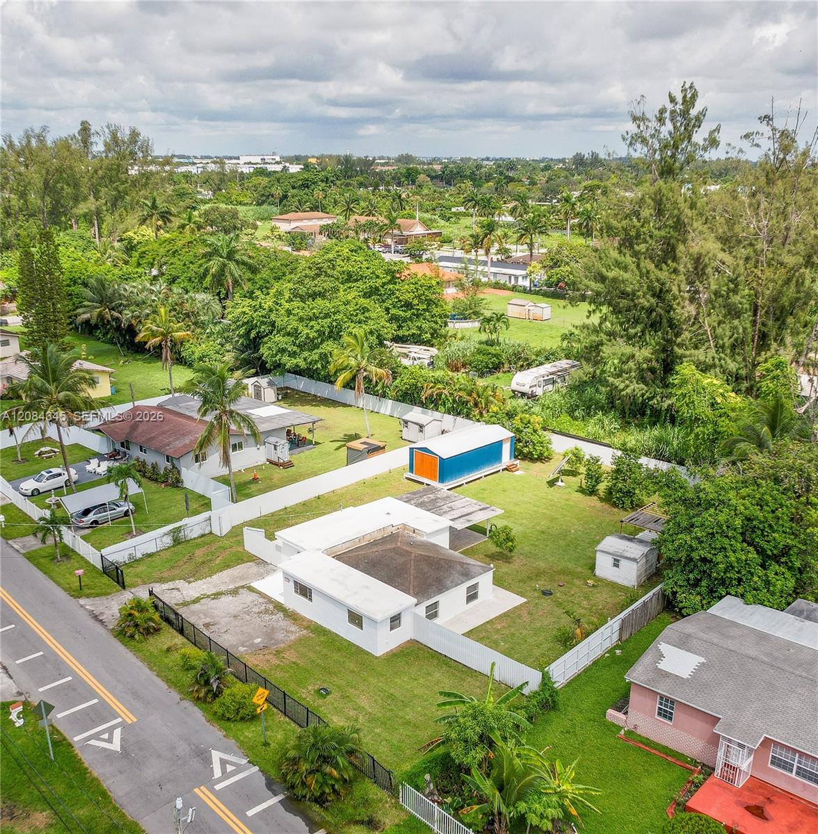 Aerial view of a white one-story home with a fenced yard and blue-and-orange shed.