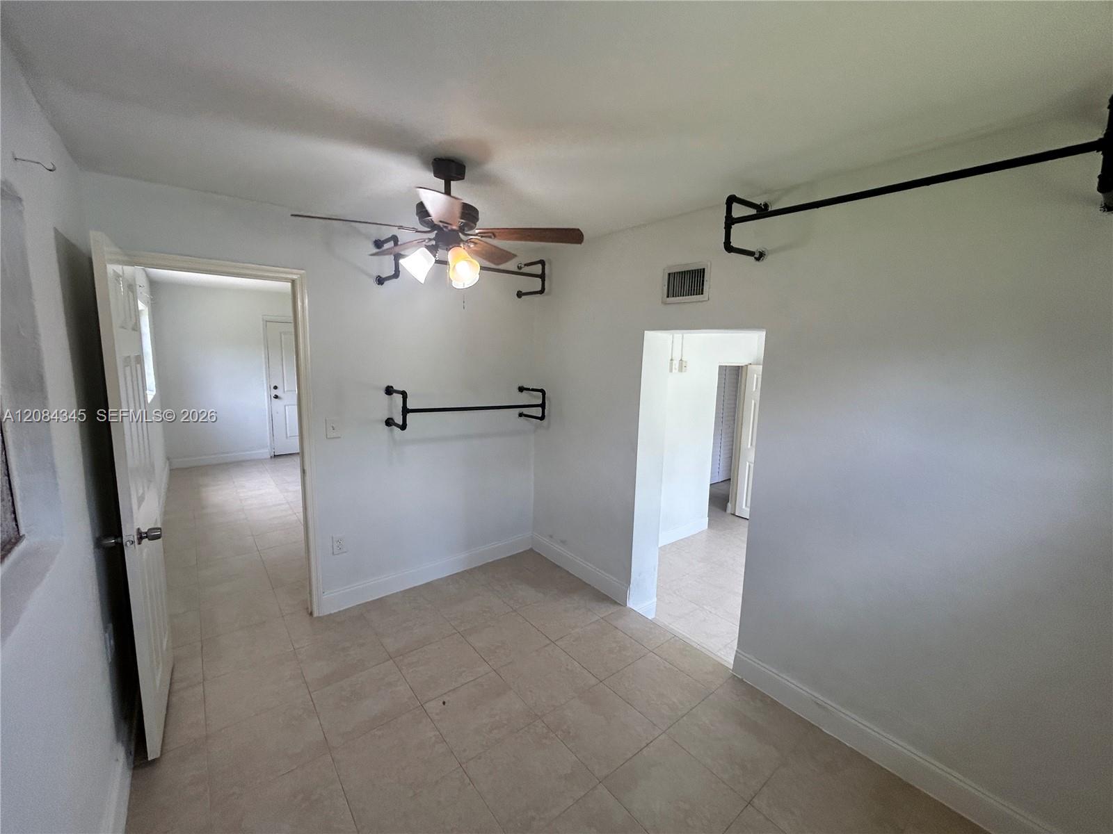 Empty tiled room with a ceiling fan, black wall racks, and open doorways.