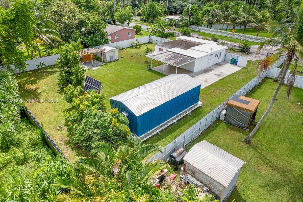 Aerial view of a fenced home and yard with a long blue metal outbuilding and palms.