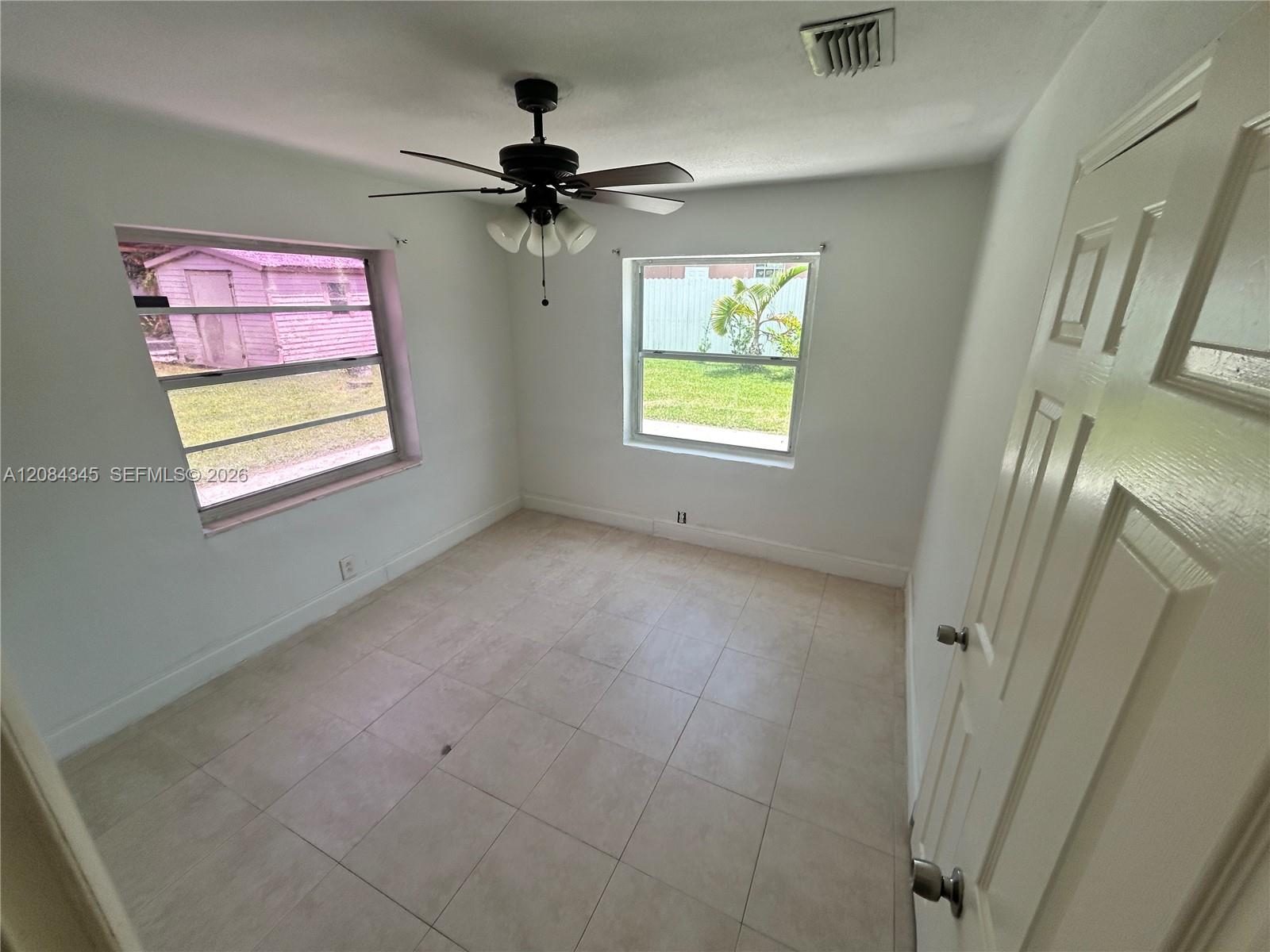 Empty tiled room with a ceiling fan, two windows, and an open paneled door.