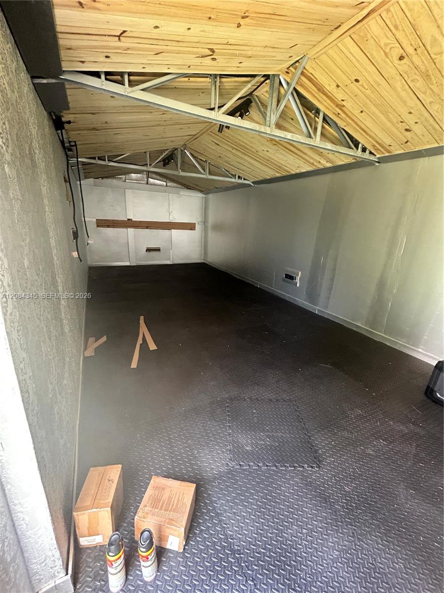 Garage with exposed wooden roof framing, metal trusses, and a dark diamond-pattern floor.