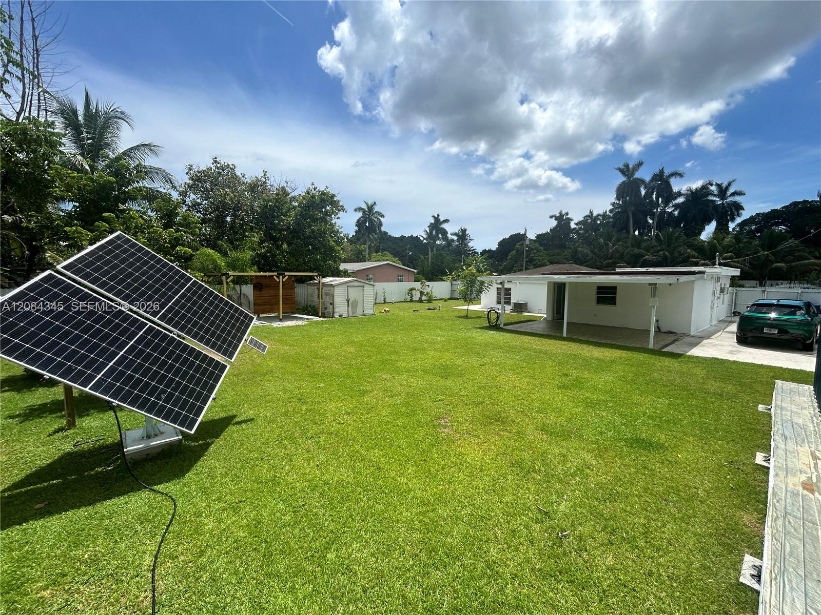 Spacious backyard with solar panels in the foreground and a single-story house beyond.