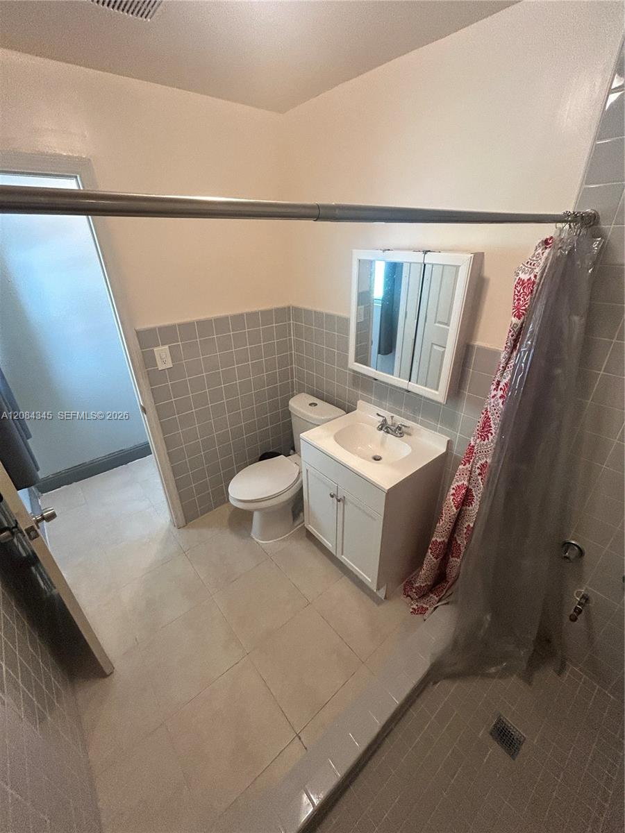 Bathroom with a white vanity and toilet, gray tile, and a red-and-white shower curtain.