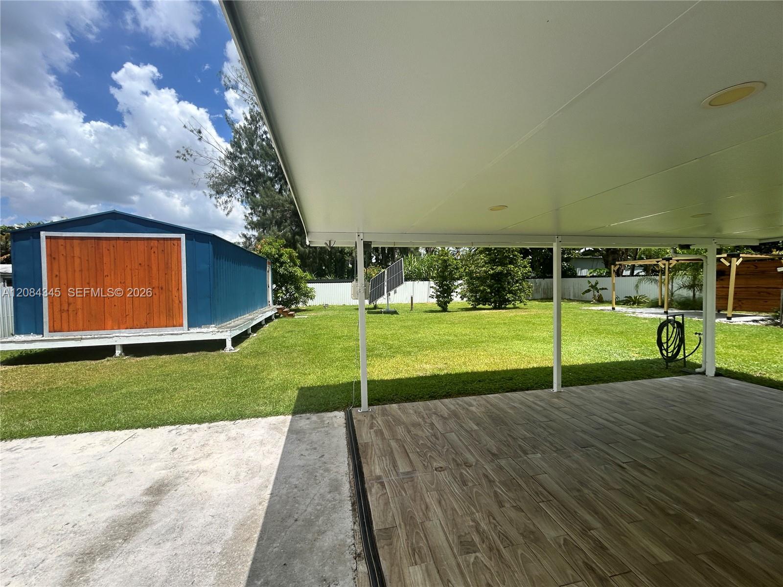 Covered tiled patio overlooking a lawn, with a blue shed and freestanding solar panels.