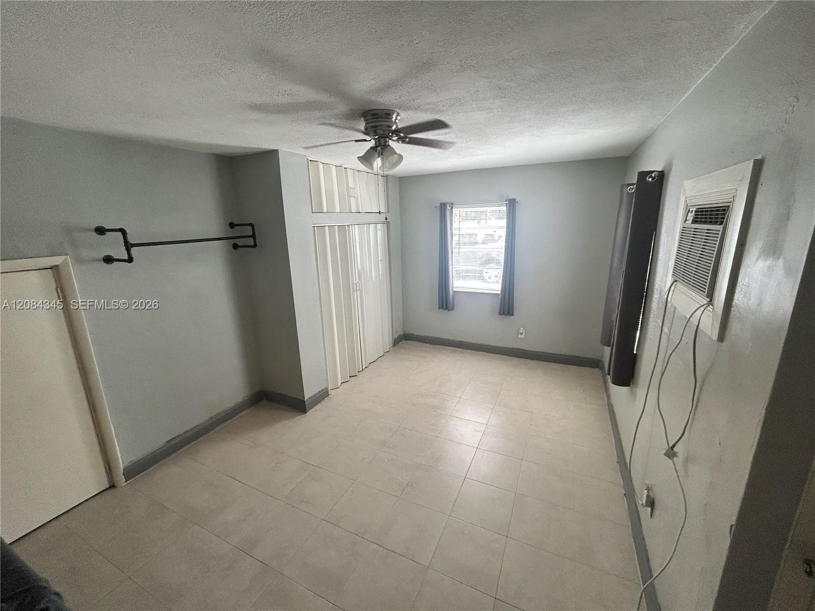 Empty bedroom with tiled floor, built-in closet, ceiling fan, and window air conditioner.