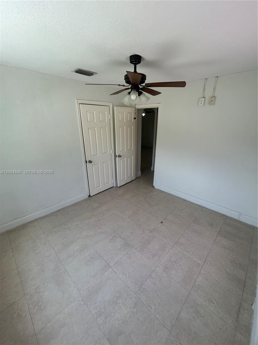 Empty bedroom with tiled floors, a ceiling fan, and two white paneled doors.