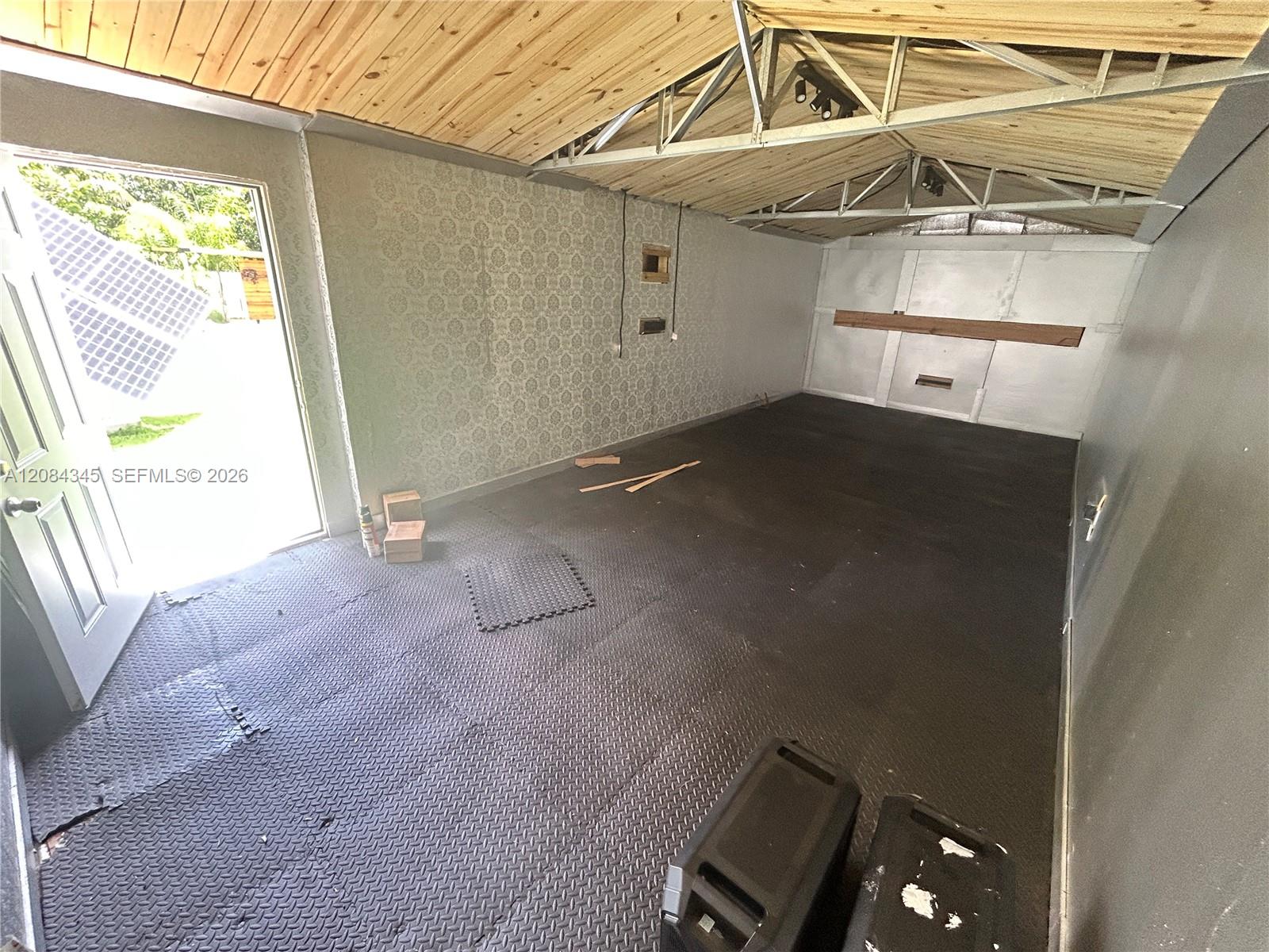 Garage with diamond-pattern flooring, exposed roof trusses, and a light wood-plank ceiling.