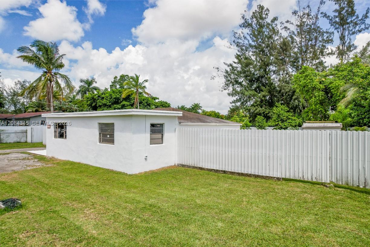 Single-story white house beside a broad lawn and long white privacy fence, with palms behind it.