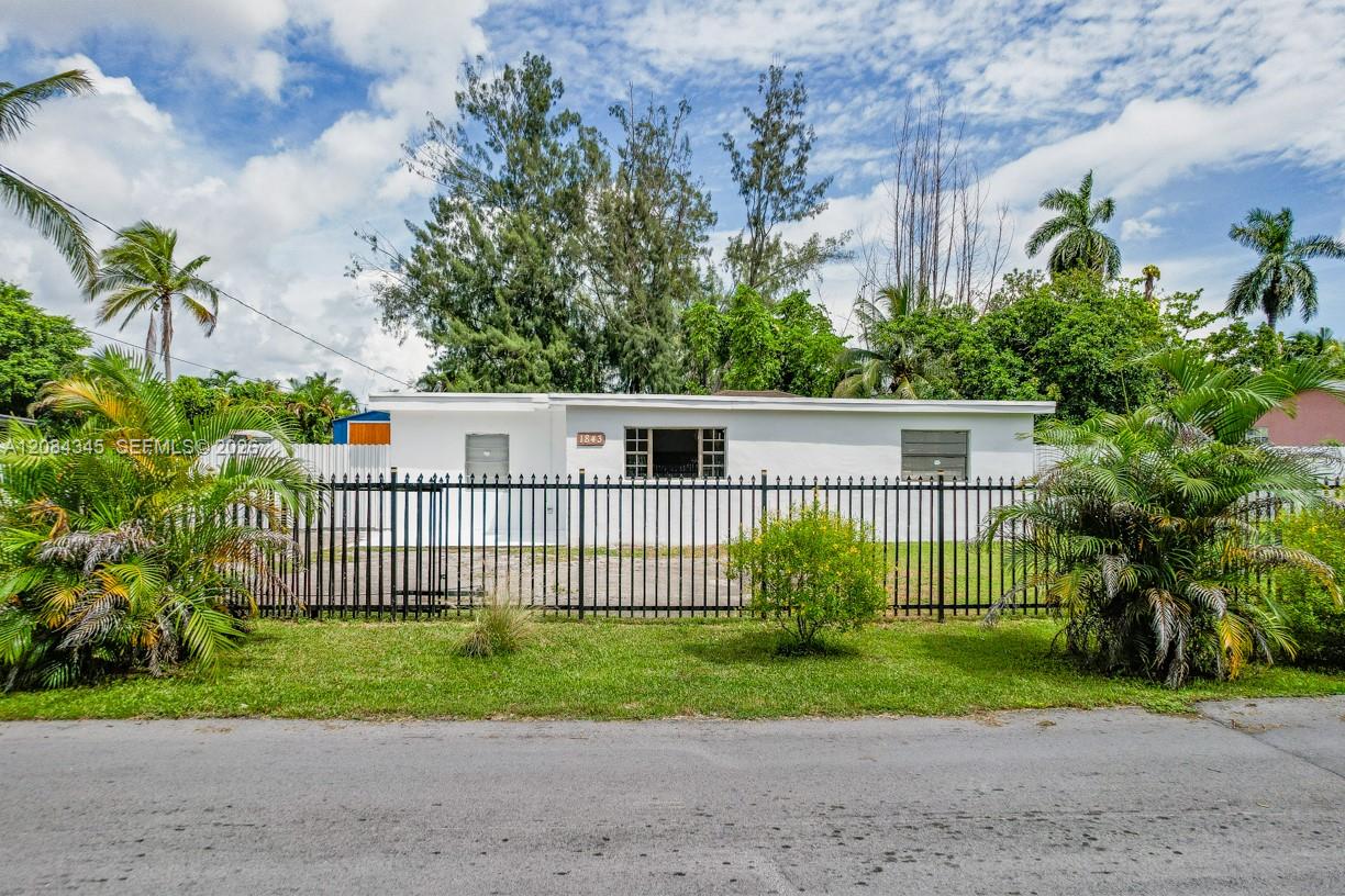 Single-story white house behind a black metal fence, framed by tropical palms and landscaping.