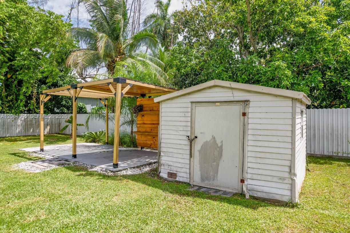Backyard with a white storage shed and wooden pergola surrounded by tropical greenery.