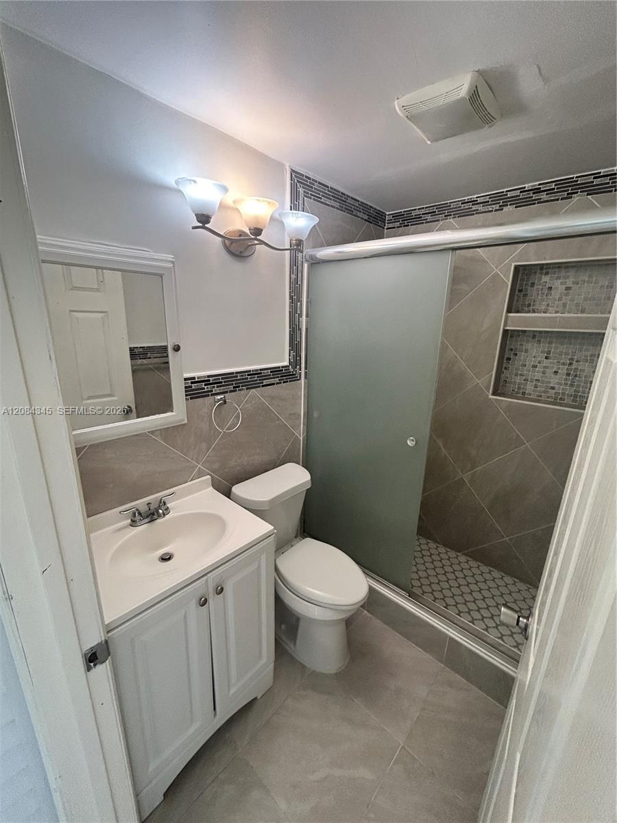 Bathroom with a white vanity, toilet, and frosted-glass shower with a tiled niche.