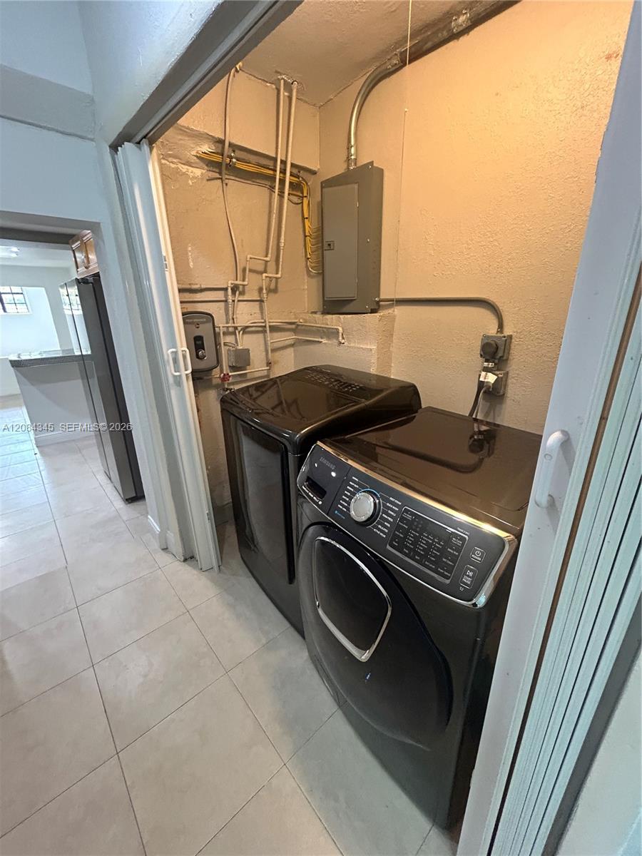 Laundry room with black front-loading washer and dryer, exposed pipes, and light tile floor.