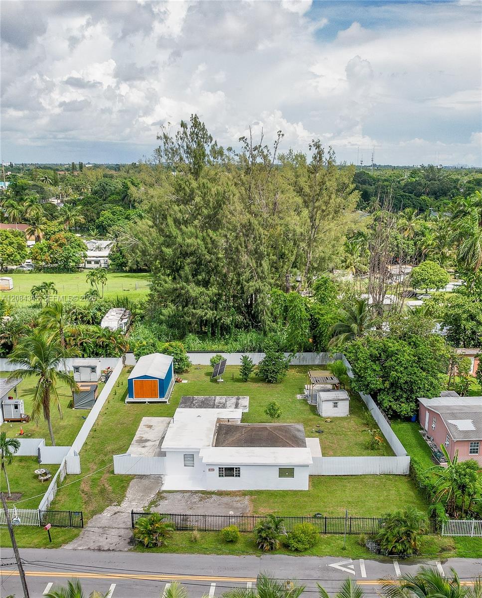 Aerial view of a white single-story property with a fenced yard, blue-and-orange shed, and mature trees.