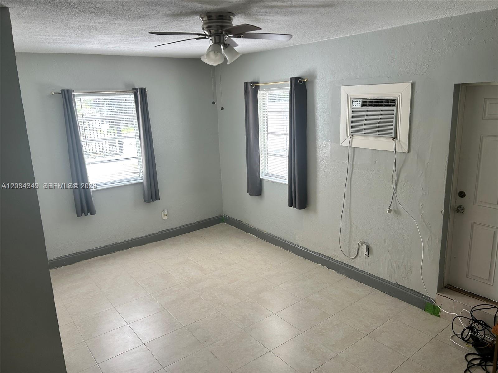 Empty tiled room with two curtained windows, a ceiling fan, and a window air conditioner.