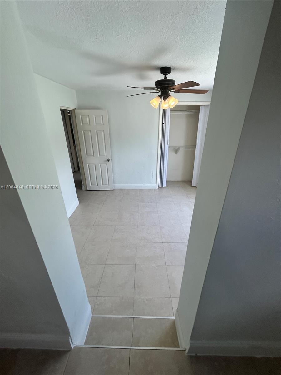 Empty room with pale tile floors, a ceiling fan, and an open closet.
