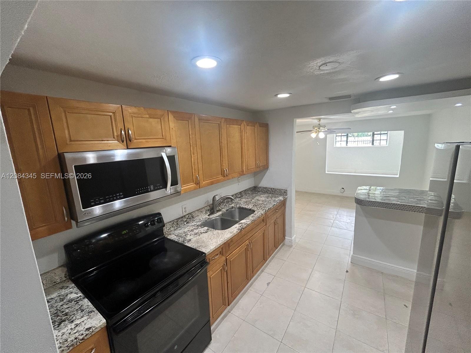 Kitchen with wood cabinets, granite counters, and black range opening into an empty tiled room.