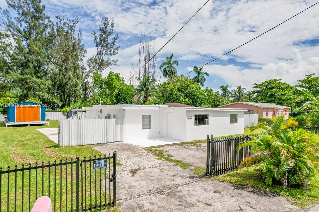 White single-story house behind a black gate, with a cracked driveway and tropical landscaping.
