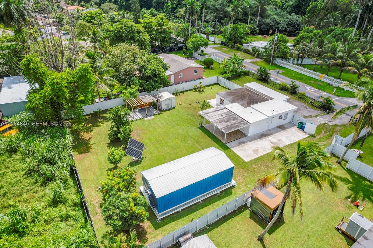 Aerial view of a fenced Miami property with a white house, blue outbuilding, and spacious grassy yard.