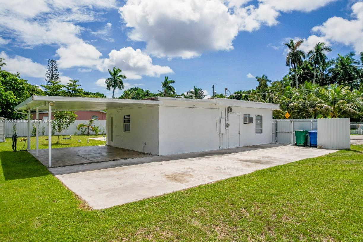 Single-story white house with a covered carport, broad driveway, and palm trees.