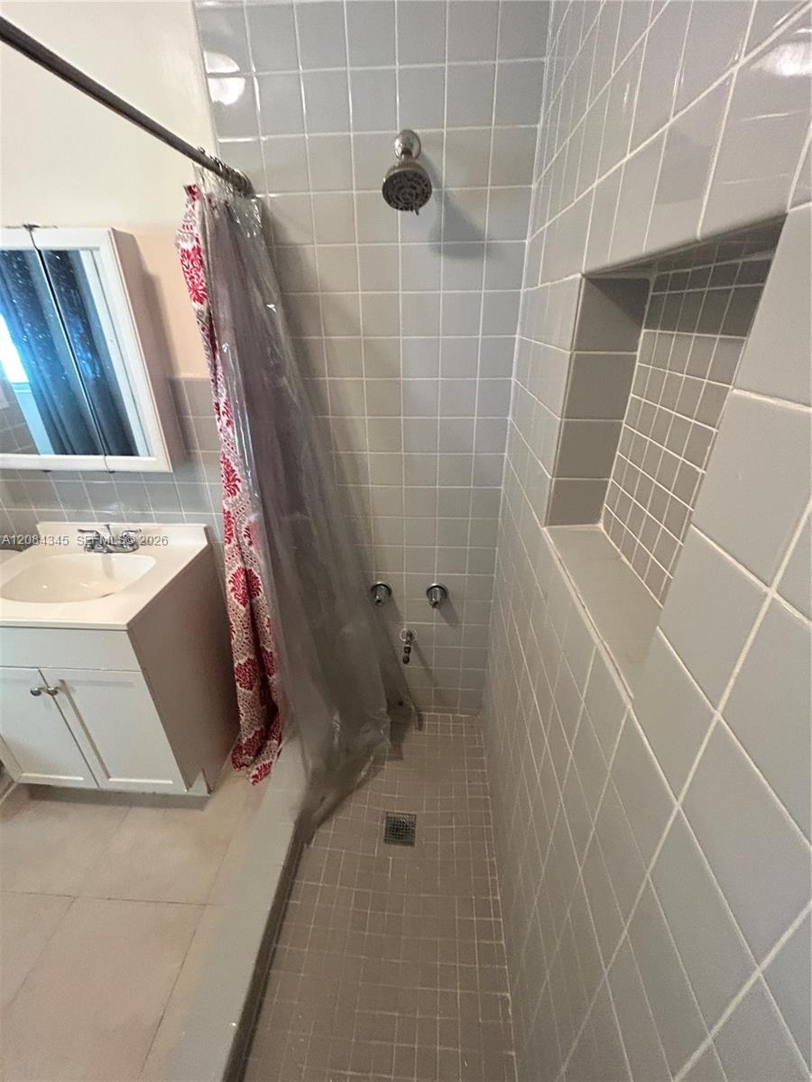 Tiled bathroom with a walk-in shower, recessed wall niche, and white vanity.