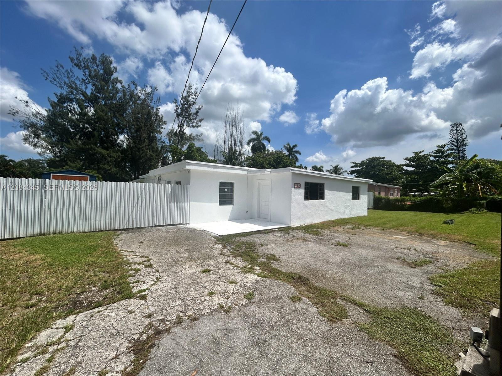 Single-story white house with a metal fence, cracked driveway, and lawn.