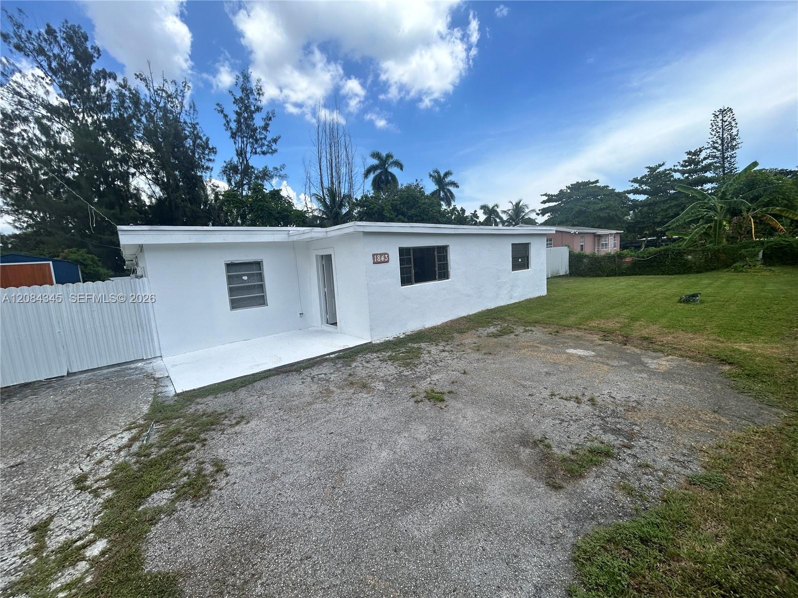 Single-story white house with a flat roof, white fence, and broad gravel driveway.