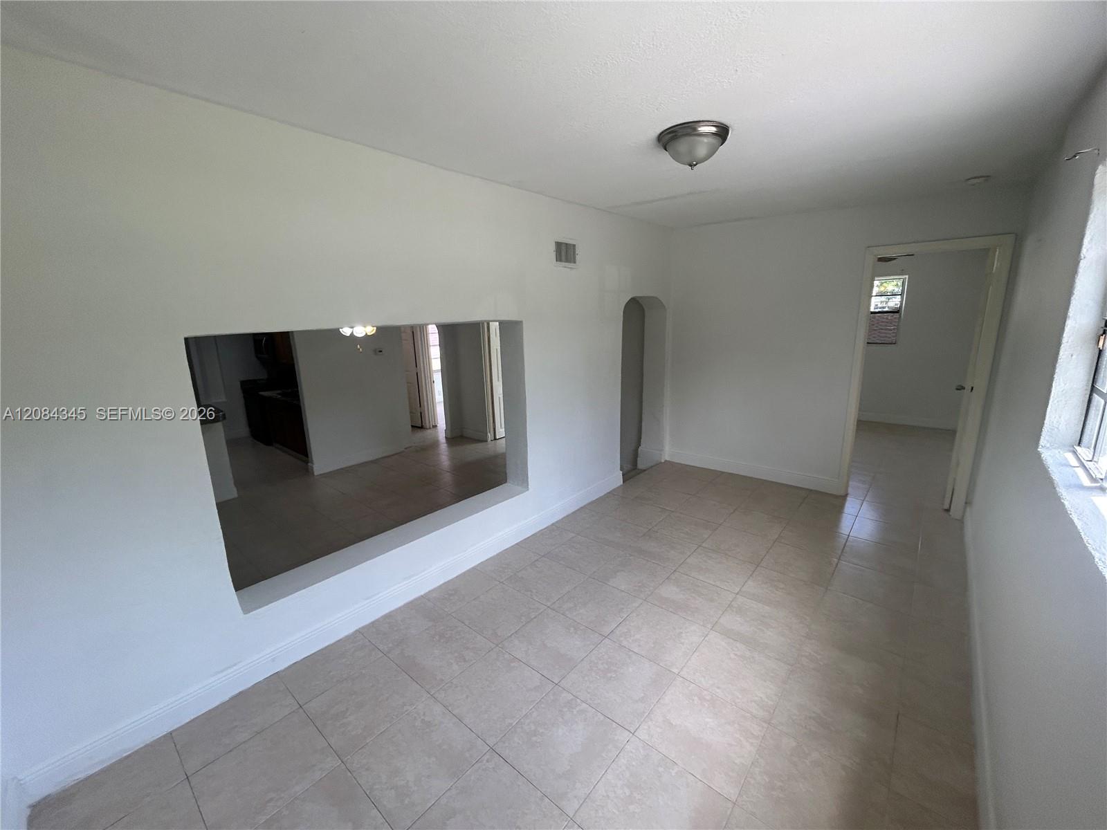 Vacant tiled living area with a wide kitchen pass-through and doorways to adjacent rooms.