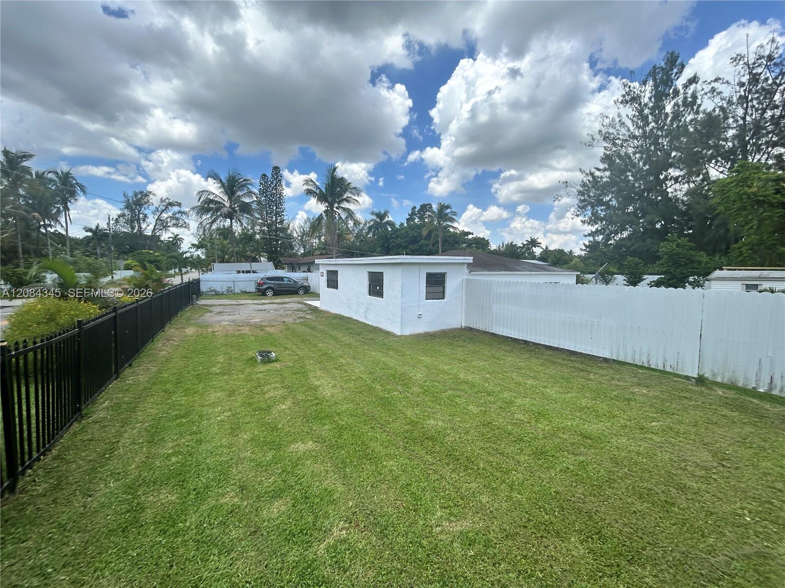 Single-story white house behind a spacious lawn, enclosed by black and white fences.