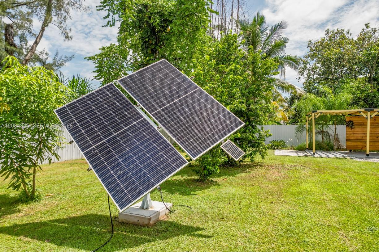 Backyard solar panels on angled mounts, surrounded by lawn, tropical trees, and a wooden pergola.