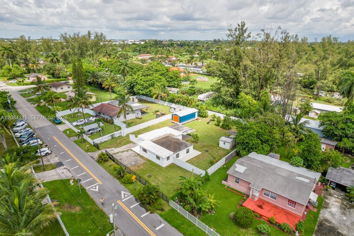 Aerial view of a white single-story home with a fenced lawn amid palm-lined Miami streets.
