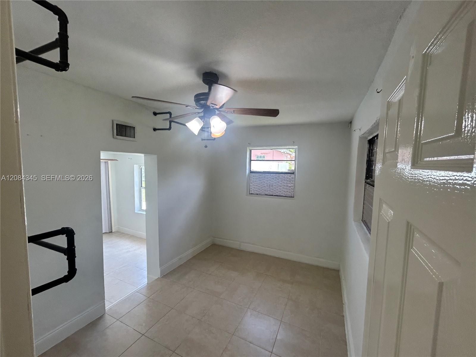 Vacant tiled room with a ceiling fan, two windows, and an open doorway.