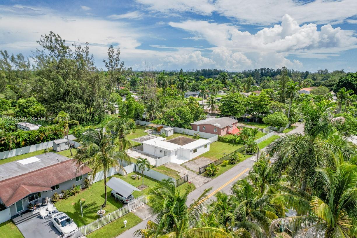 Aerial view of a white single-story house with a fenced yard among palm-lined homes.