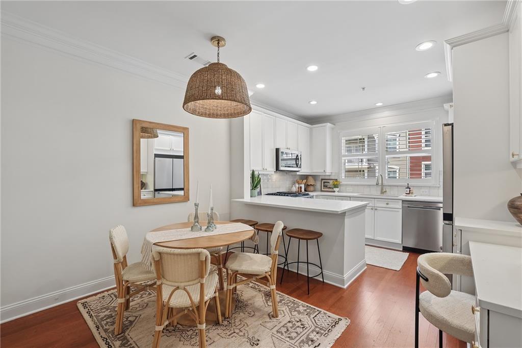 Kitchen and dining area with white cabinetry, peninsula seating, and a round table on a patterned rug.