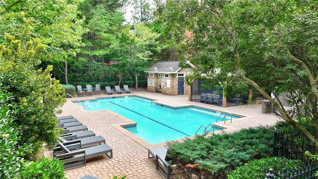 Outdoor swimming pool with brick deck, lounge chairs, and a pool house amid dense greenery.