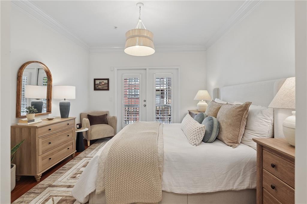 Furnished bedroom with a large neutral bed, wood dressers, and shuttered French doors.