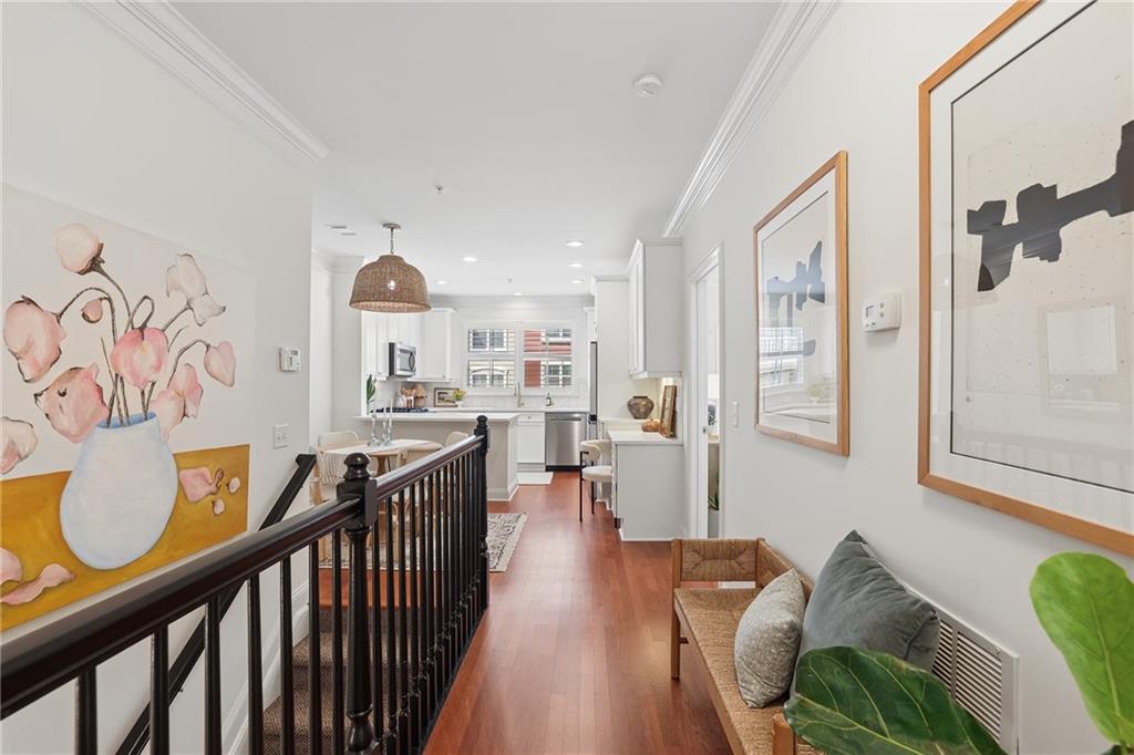 Upstairs hallway with warm wood floors, dark railing, and a view into the white kitchen.