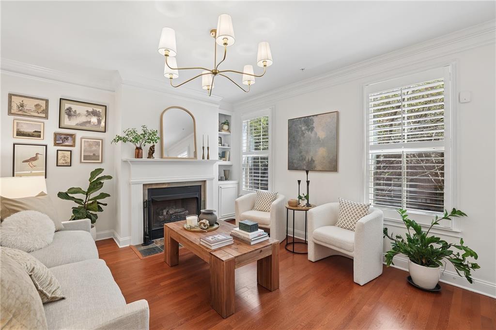 Living room with a white fireplace, hardwood floors, cream seating, and large shuttered windows.