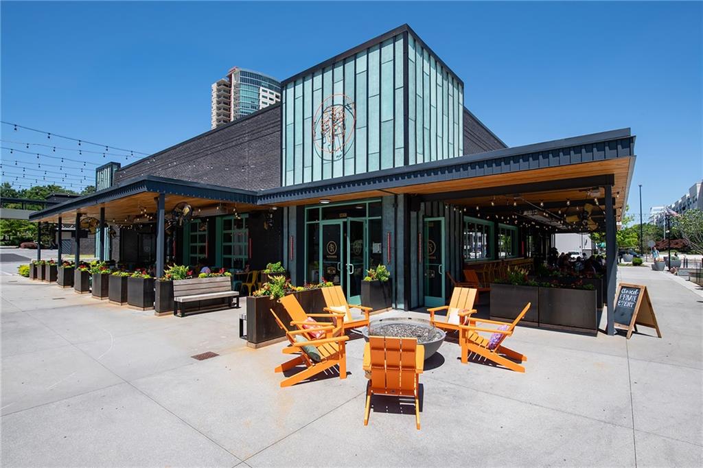 Modern glass-fronted restaurant with a covered patio and orange outdoor chairs around a fire pit.