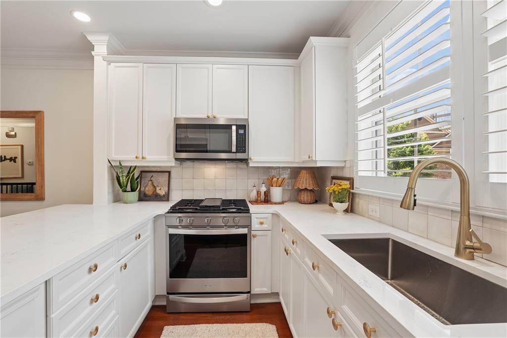 White kitchen with quartz counters, stainless steel range, and a large sink beneath shuttered windows.