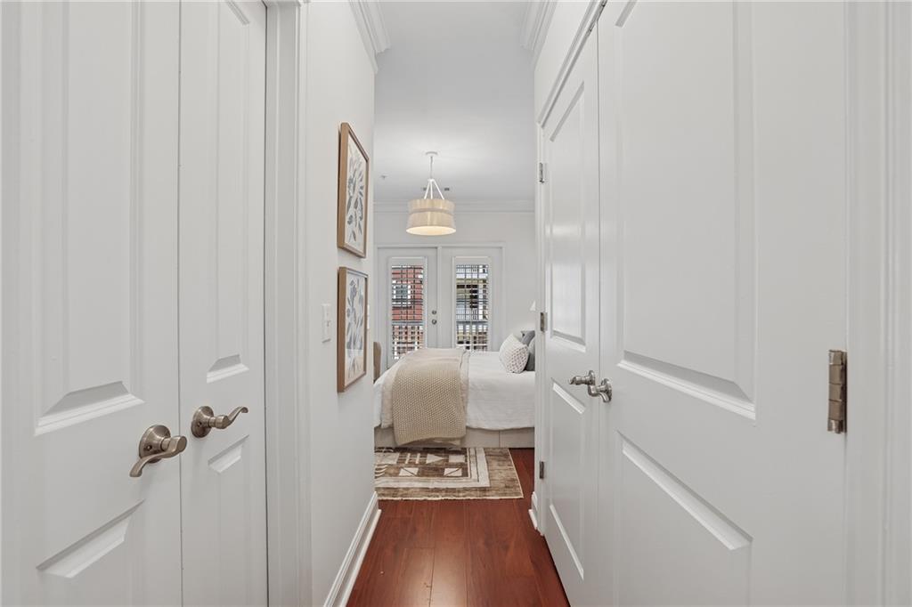 White paneled hallway leading to a bedroom with a bed and hardwood floors.
