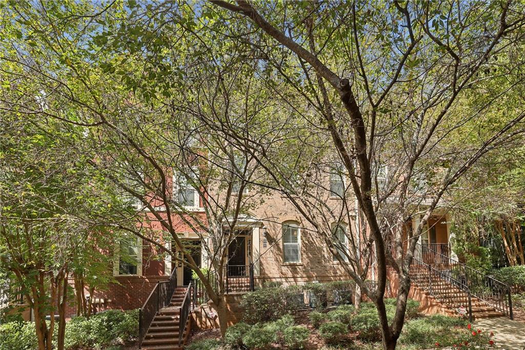 Brick home framed by mature trees, with landscaped grounds and stairways leading to the entrances.